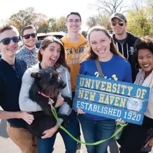 A group of students holding a sign promoting the university. 
