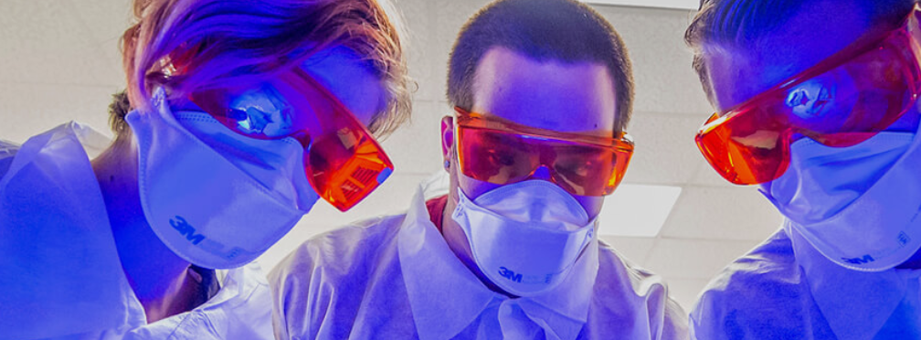 Three students conducting lab work while wearing protective equipment.